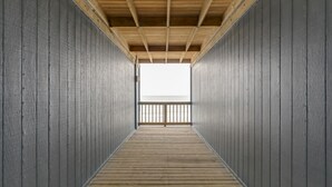 Un couloir au plancher de bois et aux murs gris, qui mène à un balcon doté d’une balustrade.