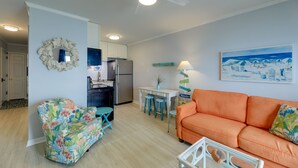Un salon comprenant un canapé, un fauteuil, une table à manger avec des tabourets, un réfrigérateur et un ventilateur de plafond.