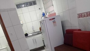 Una cuina compacta amb armaris blancs, un frigorífic i una zona de menjador amb un sofà vermell.