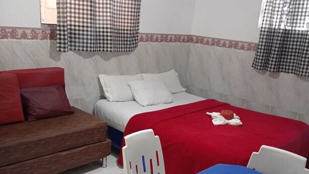 Una habitació amb llit, sofà, taula amb camavela i cadira.