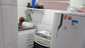 Cuina compacta amb rajoles blanques, fogó de gas, forn integrat, nevera i finestra amb persianes.
