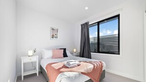 Un dormitorio ordenado con cama, mesitas de noche, una ventana con cortinas e imagen colgada en la pared.