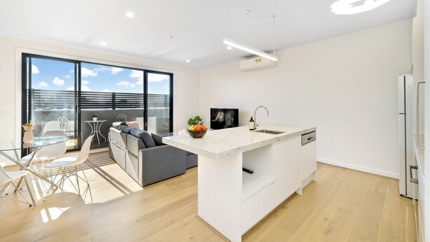 Una cocina moderna con una isla central, una zona de comedor con mesa de vidrio y un sofá gris.