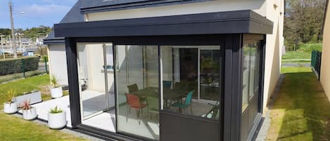 A modern house with a large glass extension, a tiled roof, and a small garden area.