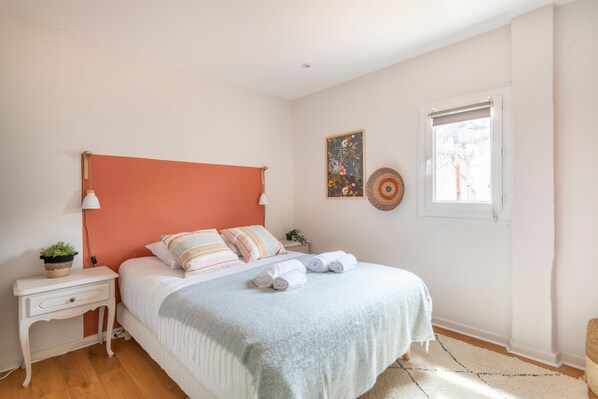 Un dormitorio con cama, mesita de noche, lámpara y ventana.