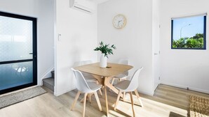 Et moderne spiseområde med et træbord, hvide stole, en potteplante og et vægur.