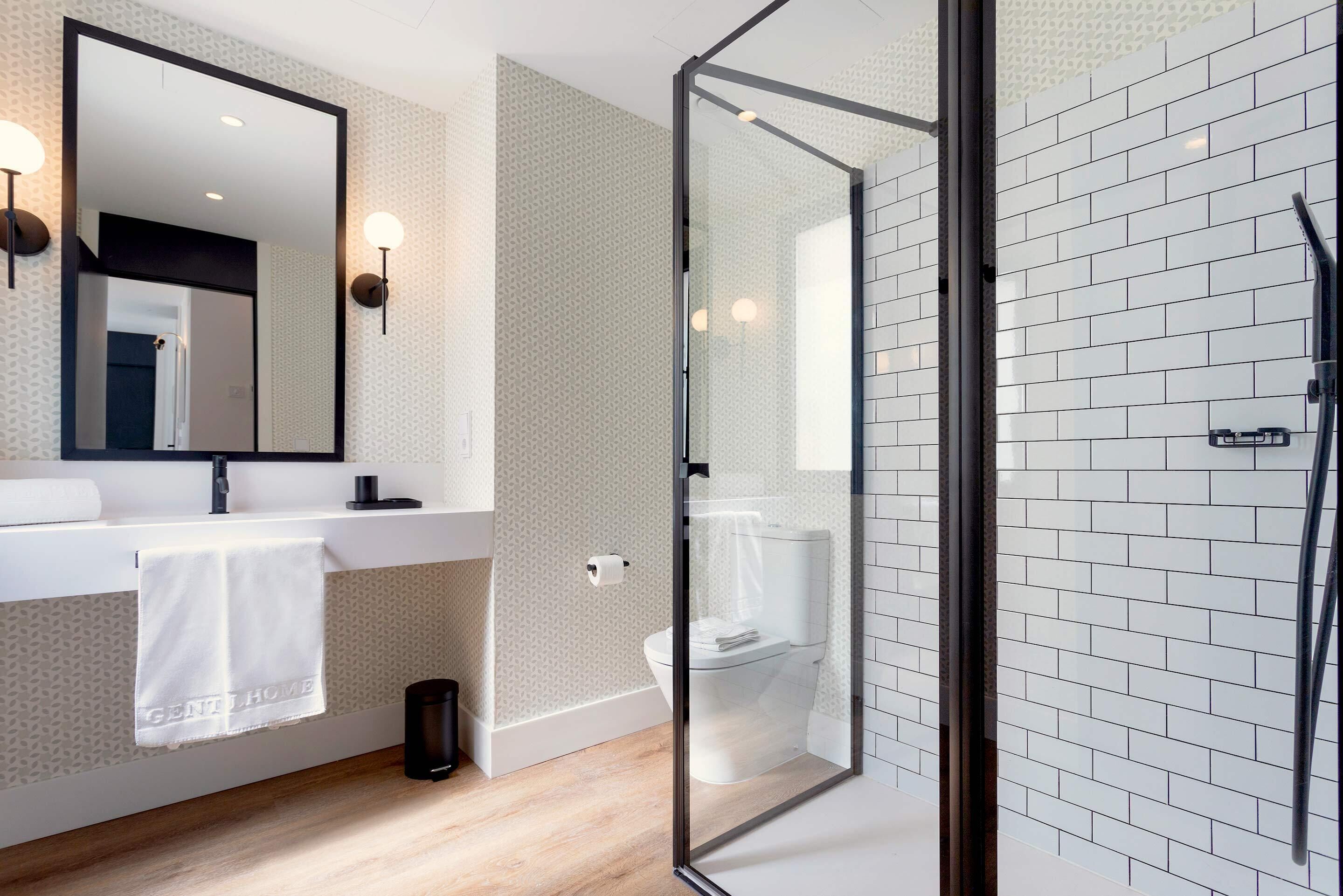 Un baño moderno con ducha acristalada, un lavamanos blanco con una toalla y un papel tapiz decorado.