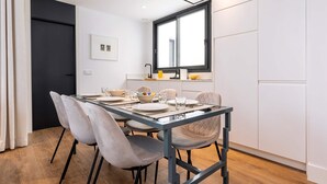 Ein moderner Essbereich mit einem Glastisch, grauen Polsterstühlen und einem Fenster mit schwarzem Rahmen.