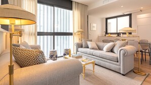 Ein modernes Wohnzimmer mit Sofa, Sessel und Stehlampe. Ein Essbereich mit Tisch und Stühlen ist ebenfalls vorhanden.