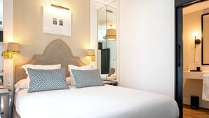 Ein ordentlich bezogenes Bett mit gemusterten Kissen, ein Nachttisch mit Lampe und ein großer Spiegel darüber.