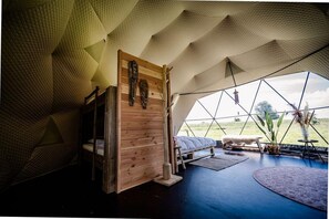 Relax in this serene geodesic dome, featuring a comfortable bed, a rustic door, and a stunning view of the surrounding landscape.