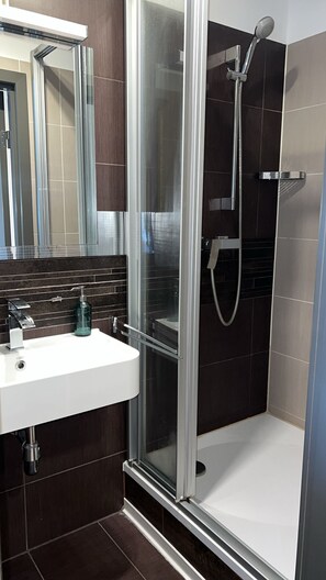 A modern bathroom with a glass-enclosed shower, a white sink with a soap dispenser, and a mirror above the sink. - Rheinländer Seehotel (Leverkusen)