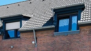 Tiilestä rakennettu rakennus, jossa on laatoitettu katto, lasiovilla varustettu vastaanottoaula ja kaksi viherkasveja sisältävää kukkaruukkua.