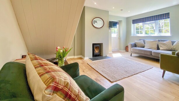 Una sala de estar con chimenea, un sofá, un sillón verde y un ventanal grande.