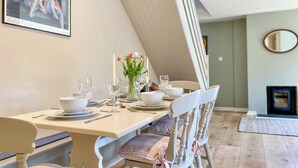 Un comedor con una mesa lista para cuatro, sillas blancas, un florero con flores y un cuadro en la pared.