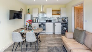 Cocina compacta con zona de comedor, sofá y televisor montado en la pared.