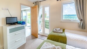 Un dormitorio con cama, televisor en una cómoda, ventana con cortinas y vistas al exterior.
