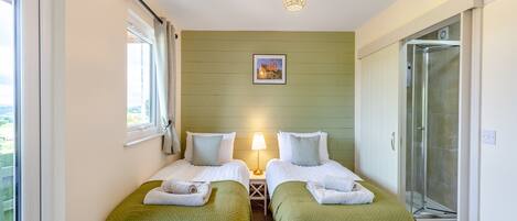A bedroom with two beds, a window, a lamp, and a shower.
