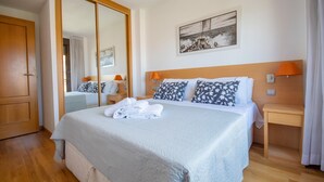 A neatly made bed with a white comforter and pillows, a wooden headboard, a bedside table with a lamp, and a large mirror.