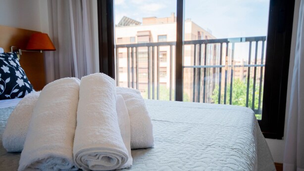 A neatly made bed with rolled white towels and a white quilted bedspread.