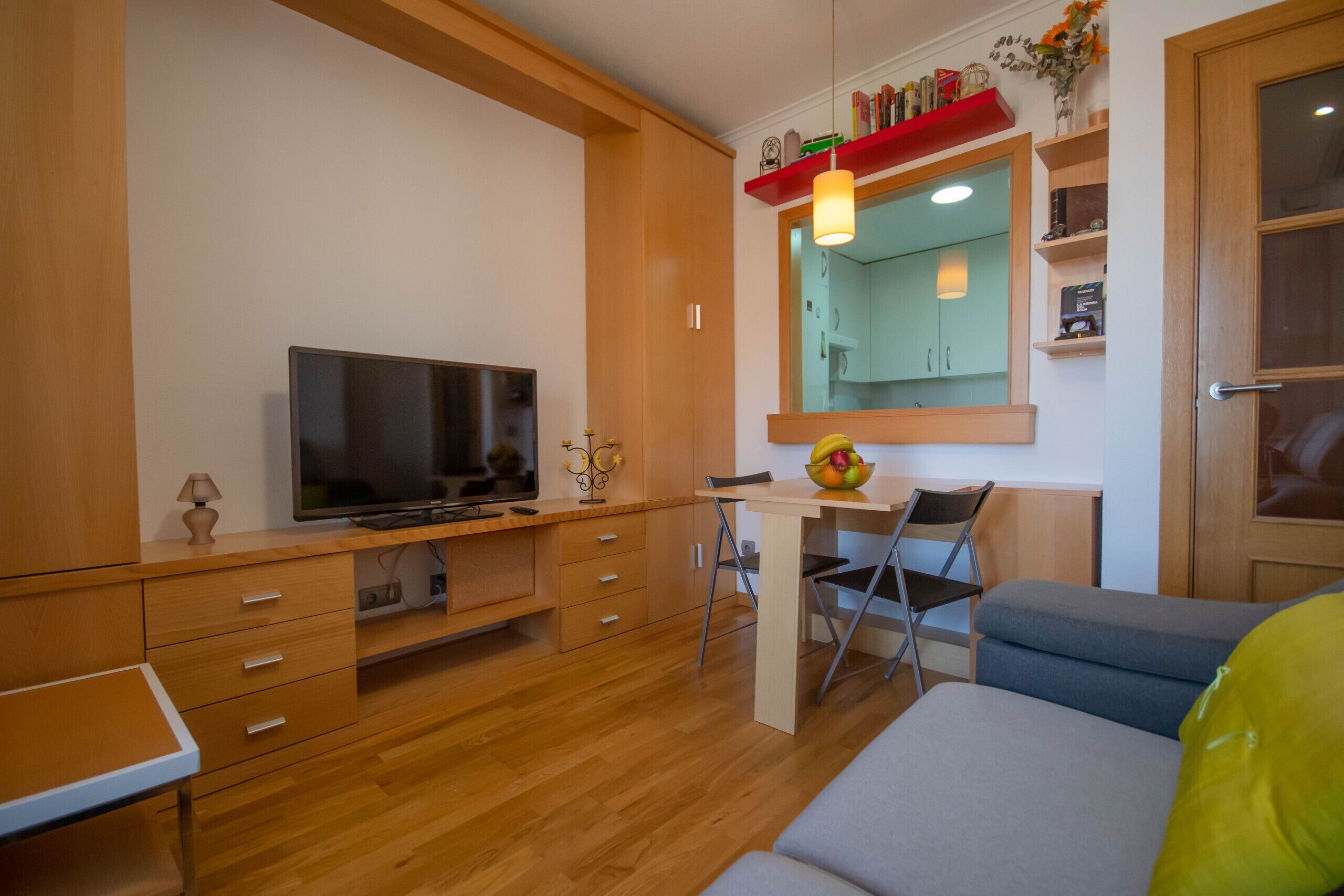 A compact living space with a TV, wooden furniture, a small dining table, and a sofa.