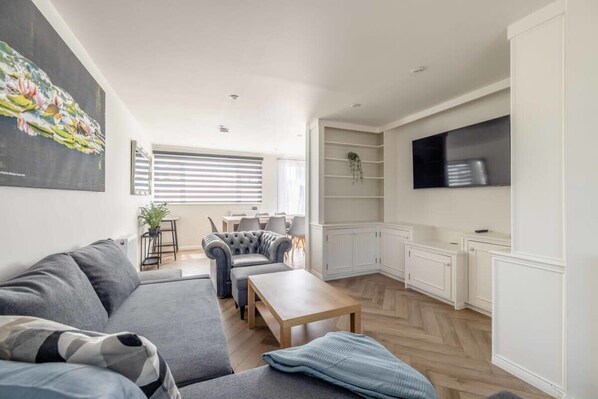 A modern living room with a grey sofa, a wooden coffee table, and a dining area with a grey upholstered chair.