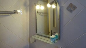 Un baño con barandilla, un espejo con iluminación y un estante con artículos de tocador.