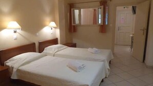 A hotel room with two beds, a bathroom with a shower, and a door leading to another room. - Aronis Studios Triple bed with View & Patio 03 (Kapsáli)