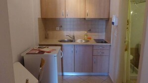 A compact kitchen with wooden cabinets, a sink, and a small refrigerator. - Aronis Studios Triple bed with View & Patio 03 (Kapsáli)