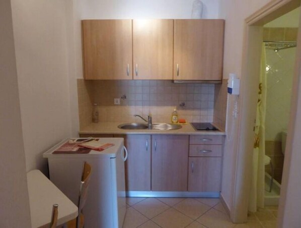 Una cocina compacta con muebles de madera, un lavamanos y un refrigerador pequeño.
