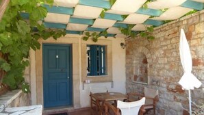 A covered outdoor seating area with a stone wall, a blue door, and a white umbrella. - Aronis Studios Triple bed with View & Patio 03 (Kapsáli)