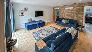 A modern living room with a blue sofa set, a flat-screen TV, and a brick accent wall.