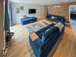 A modern living room with a blue sofa set, a flat-screen TV, and a brick accent wall. - No. 1 Fox Burrow-UK44306 (Great Witchingham)