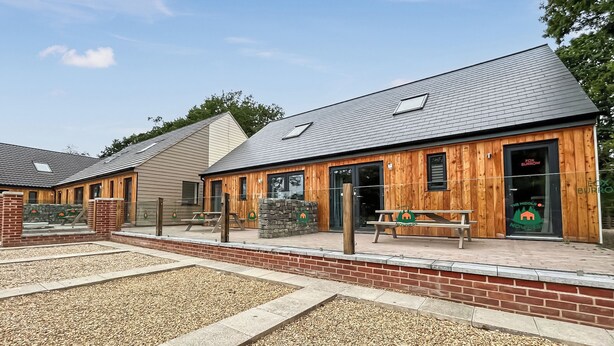A building with a wooden exterior, a stone wall, and a gravel courtyard.