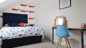 A bedroom with a bed, a desk, a chair, a wall decal of animals, a pendant light, and a motivational quote on the wall.
