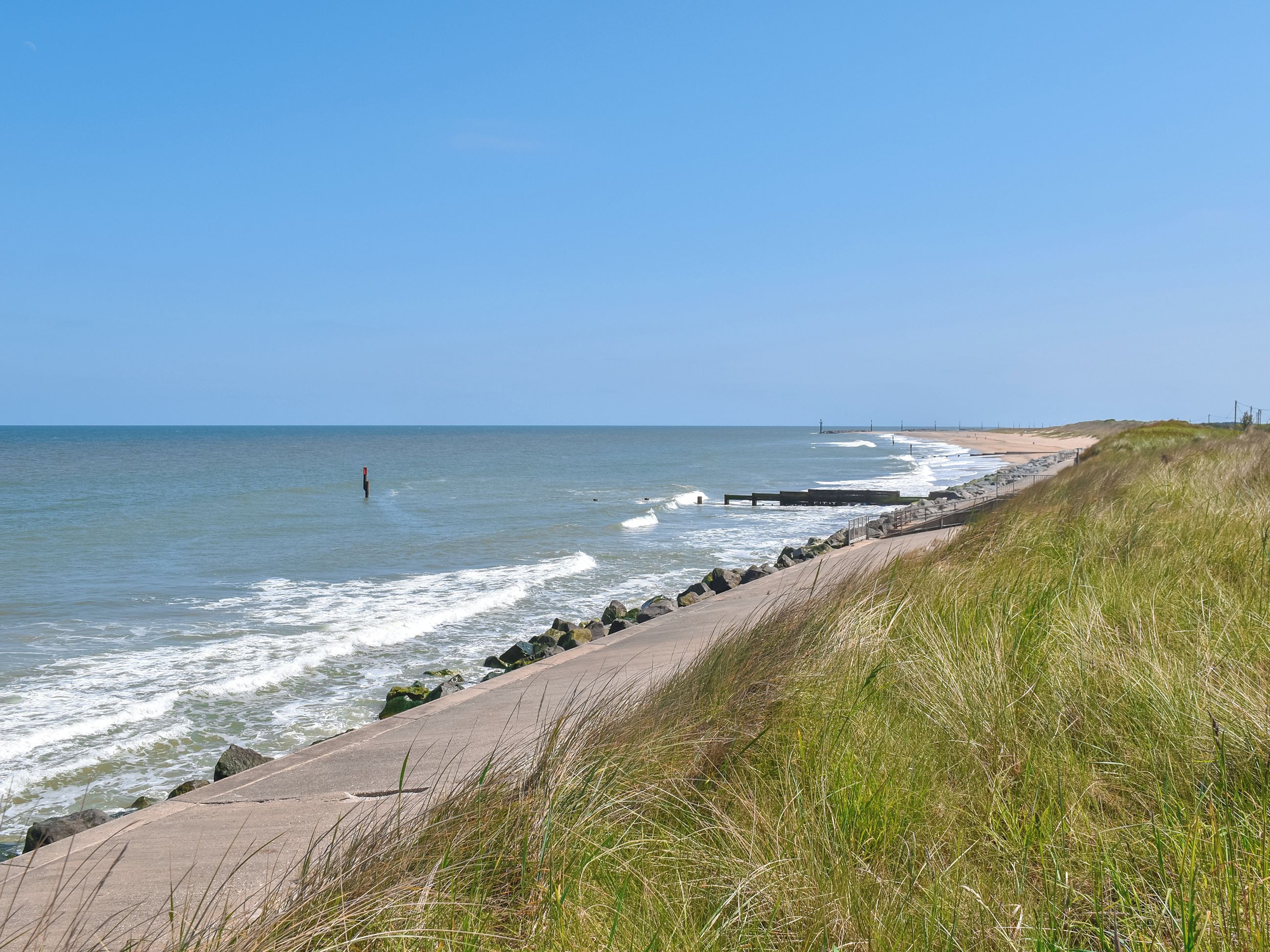 A coastal walkway with a concrete path, grassy areas, and a clear view of the ocean.