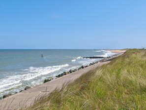 A coastal walkway with a concrete path, grassy areas, and a clear view of the ocean. - No. 1 Fox Burrow-UK44306 (Great Witchingham)