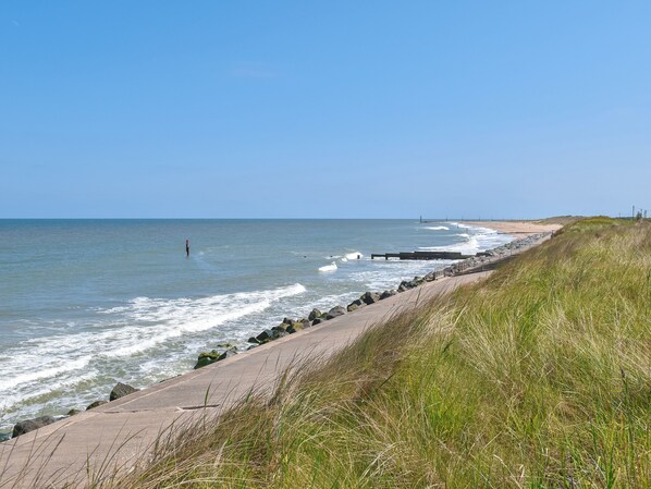 A coastal walkway with a concrete path, grassy areas, and a clear view of the ocean.