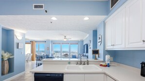 A kitchen with white cabinets, a dishwasher, and a large window overlooking a balcony.