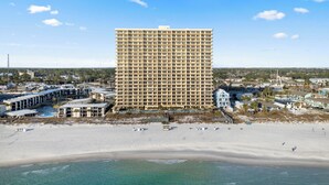 A high-rise hotel with a uniform facade, located adjacent to a sandy beach and a body of water.