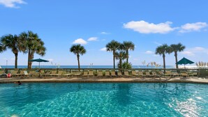 A clear blue pool with lounge chairs and palm trees, overlooking a beach.