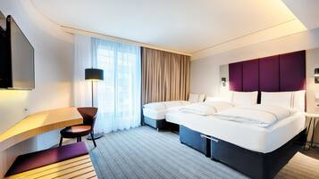 Ein modernes Hotelzimmer mit einem Bogenförmigen Schreibtisch, einem Bett mit Kopfteil, einem Sessel, einem Nachttisch und einem großen Fenster mit Vorhängen.