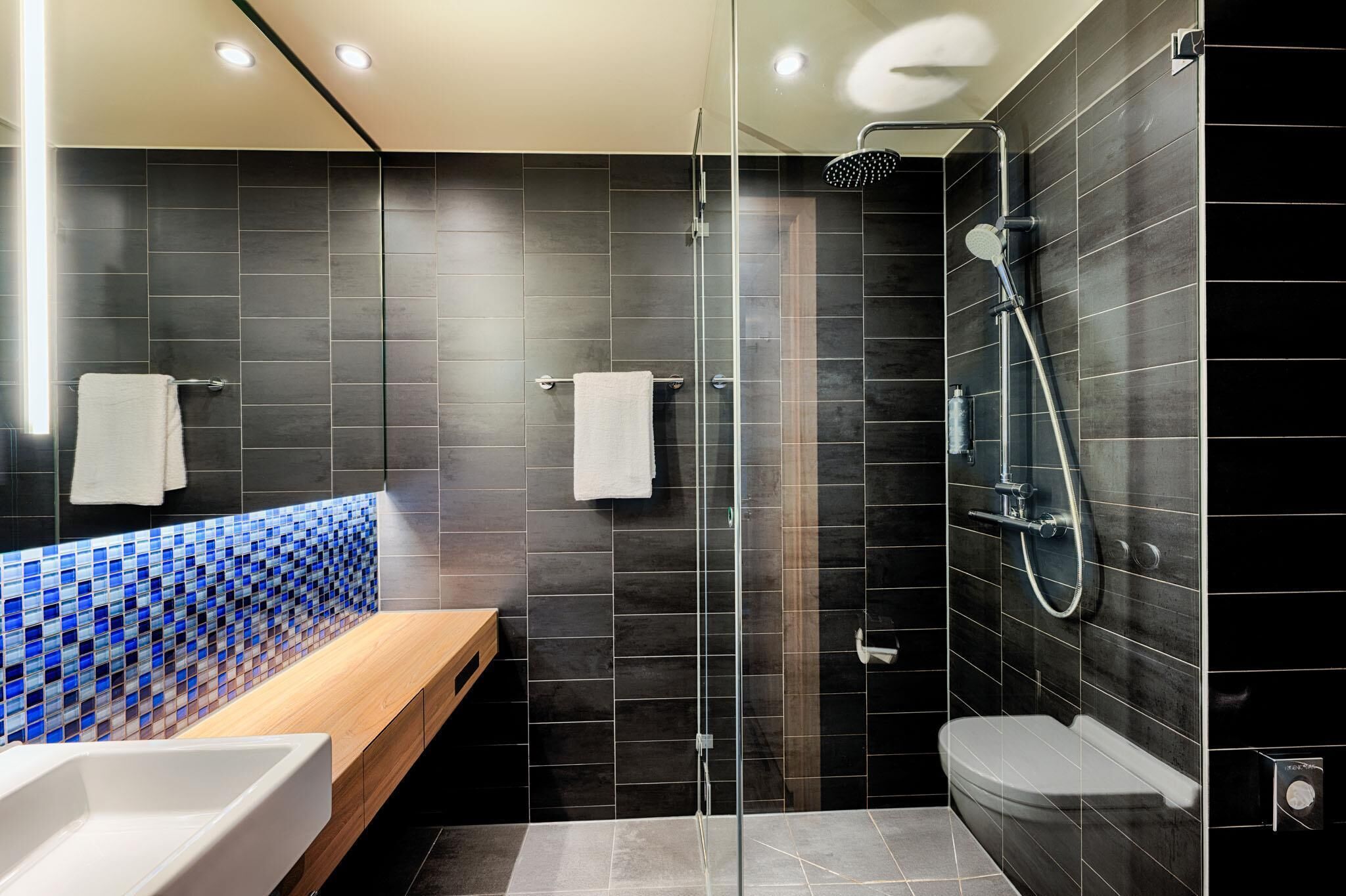 Een moderne badkamer met een douchecabine van glas, een houten wastafelmeubel en een betegelde spatwand.