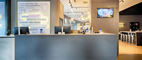 A hotel reception desk with a large screen displaying text and a television above it.