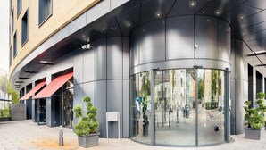 A modern building with a curved entrance, glass doors, and a red awning. - Premier Inn Heilbronn City Centre (Heilbronn)