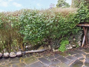 En sti af sten fører hen til et træbord, omgivet af frodig grøn vegetation og en stenvæg.