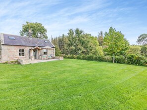 A stone house with a sloped roof, a patio with outdoor furniture, and a well-maintained lawn. - 1 bedroom accommodation in Eglingham, near Alnwick (Eglingham, near Alnwick)
