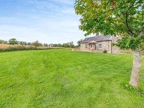 Une maison en pierre avec une grande pelouse et un arbre au premier plan.