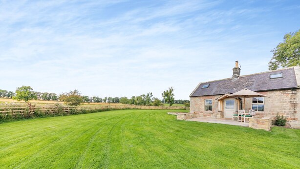 A stone house with a large lawn, a patio with outdoor seating, and a chimney.