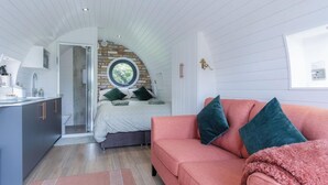 A compact bedroom with a lofted sleeping area, a pink sofa, and a small kitchenette. - Woody's - 1 Bedroom Pod - Cold Inn (Kilgetty)